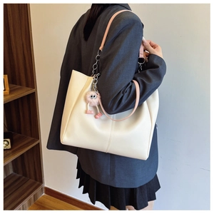 Detail view of cream tote bag featuring pink leather chain strap and plush ball charm