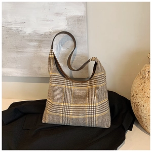 Detailed close-up of houndstooth plaid tote bag with brown faux leather strap on black blazer