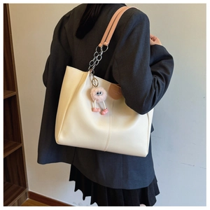 Detailed back view of a cream tote bag with metal chain strap and pink plush charm