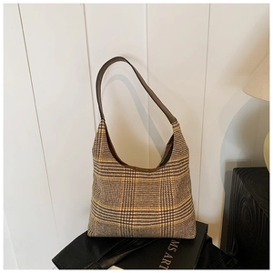 Detailed close-up of brown plaid hobo bag with wide leather strap on art book background
