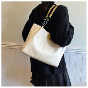 Model showing large beige tote bag with chain strap and vertical stitched detail
