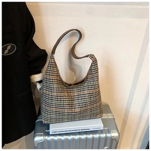 Detailed view of plaid wool hobo bag on books and silver suitcase with chic style