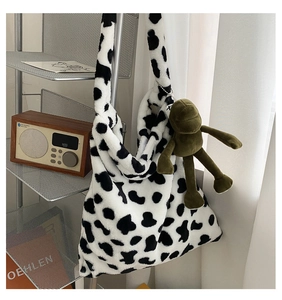 Detail of plush cow print shoulder bag with a cute green frog charm accessory
