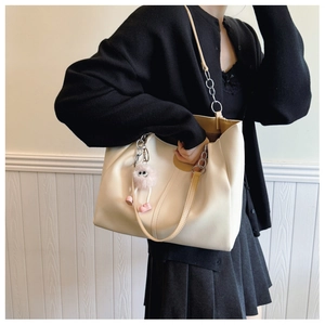 Detail of cream tote bag featuring silver chain strap and pink plush charm accessory