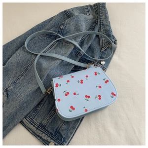 Nahaufnahme der hellblauen Umhängetasche mit Kirschmuster auf Denim-Hintergrund