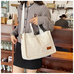 Detail of a large off-white corduroy tote bag featuring multiple pockets and a logo patch