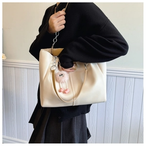 Detail of cream leather tote bag with brown straps, silver chain and pink plush charm