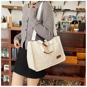 Detail view of cream corduroy tote bag with brown leather handles in a cafe setting