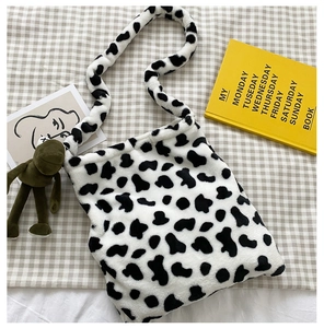 Detail of soft cow print plush handbag with green cartoon pendant on plaid background