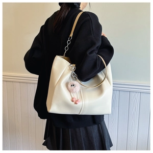 Detail of cream tote bag with metal chain strap and pink plush charm on model