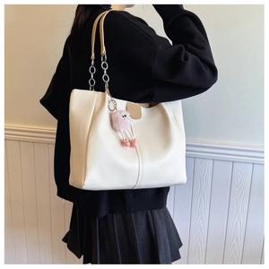 Detail of off-white tote bag featuring ruched texture and metal chain strap with pink charm