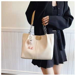 Detail view of cream tote bag featuring silver chain straps and a pink plush charm