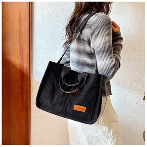 Detail of black corduroy tote bag showing the texture, fashion patch and brown leather handle