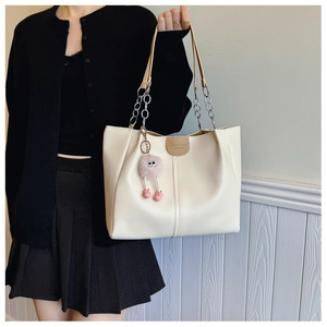 Detail of cream white tote bag with chain strap, leather tag, and pink monster charm