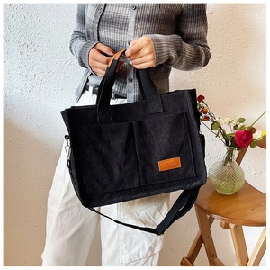 Detail of black corduroy tote bag showing side pockets and fashion leather label