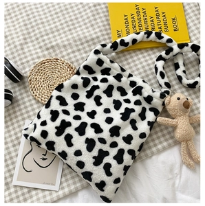 Detail of cow print plush crossbody bag featuring fluffy texture and teddy bear charm