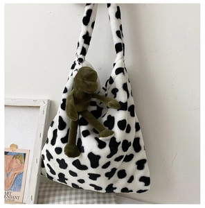 Close-up of fluffy cow print plush bag with a cute green frog charm in a cozy setting