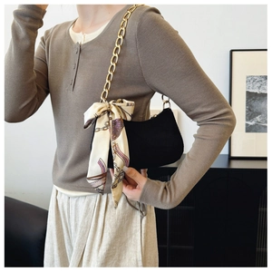Detalle de bolso medialuna negro con cadena dorada y pañuelo de seda decorativo