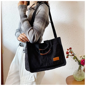 Detail of black corduroy tote bag showing front pockets and leather logo on white background