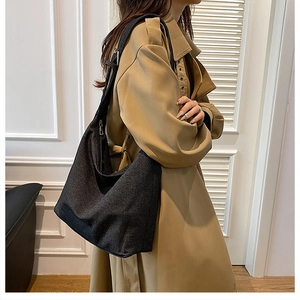 Grand sac hobo noir en denim porté avec un trench-coat kaki pour un look décontracté