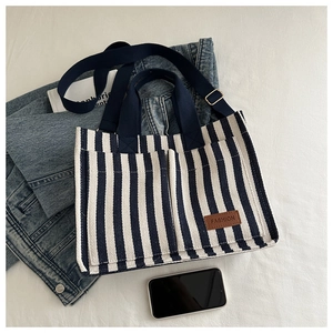 Detail of blue striped canvas tote bag showing front pockets and leather logo patch