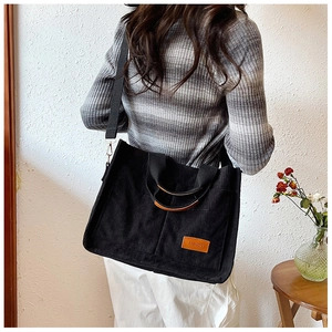 Detail shot of black corduroy tote bag featuring a leather fashion label and wide strap