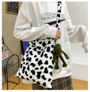 Detail of plush cow print crossbody bag with cute green frog charm in a cozy setting