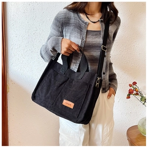Close-up of black corduroy tote bag with fashion label and adjustable shoulder straps