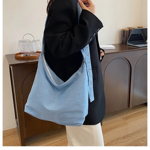 Détail du grand sac cabas en jean bleu clair avec bandoulière à œillets métalliques