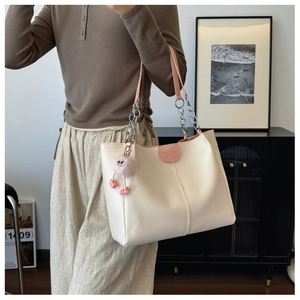 Close-up of cream PU leather tote bag with pink straps and plush pom-pom charm