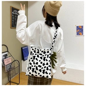 Model wearing a plush cow print crossbody bag with a cute green frog pendant detail