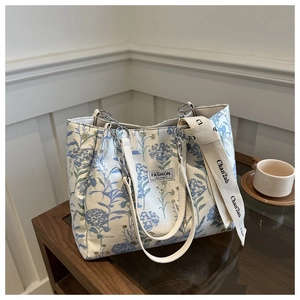 Detail of blue floral tote bag with silver chain and wide beige branded textile strap