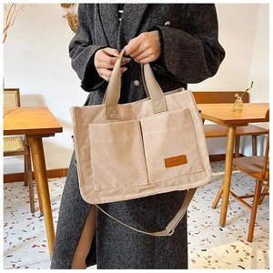 Detail of corduroy tote bag featuring front pockets, leather patch and woven handles