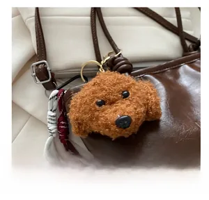 Brown poodle plush charm with curly fur and golden ring buckle hanging on a leather bag