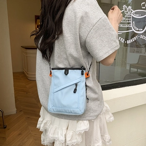 Detail of light blue crossbody bag with front zipper and athletic cord strap outdoors