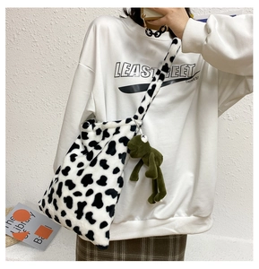Detail of plush cow print crossbody bag featuring a green frog charm on the side strap