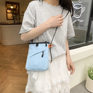 Detailed shot of a light blue nylon crossbody bag featuring contrast orange accents on the strap