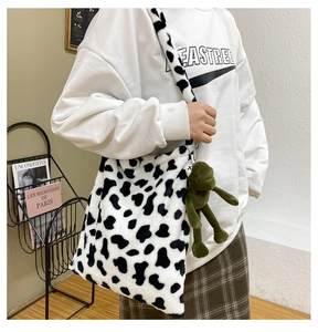 Detail of cow print plush crossbody bag with cute green frog pendant accessory