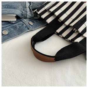 Detailed close-up of striped canvas tote bag featuring leather handles and side pocket