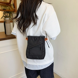 Detail view of black nylon crossbody bag with orange accents and striped cord strap on a model