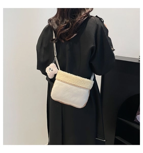 Close-up of cream fuzzy crossbody bag with plush puppy charm worn over a long black coat