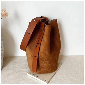 Macro shot of brown suede bucket bag with smooth leather strap on a minimal background