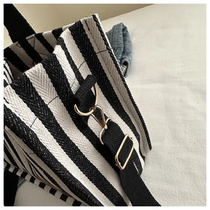 Detail view of the black and white striped canvas tote with gold-tone metal D-ring and lobster clasp