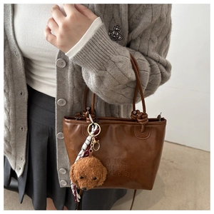 Close-up of brown retro handbag featuring letter embossing and a cute teddy bear pendant