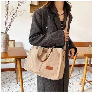 Detail of beige corduroy tote bag showing front pockets and brown leather fashion tag
