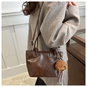 Brown leather tote bag featuring letter embossing and a cute plush dog pendant detail