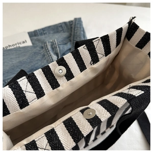 Detail view of canvas tote bag showing magnetic silver buckle and black white stripes