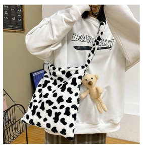 Detail of cow print plush crossbody bag featuring a cute brown teddy bear pendant charm