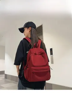 Detail view of a dark red nylon backpack with zipper pocket shown on a model
