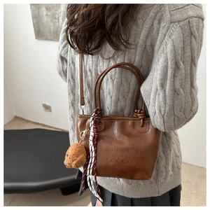 Detail of vintage brown tote bag with embossed lettering and plush dog charm